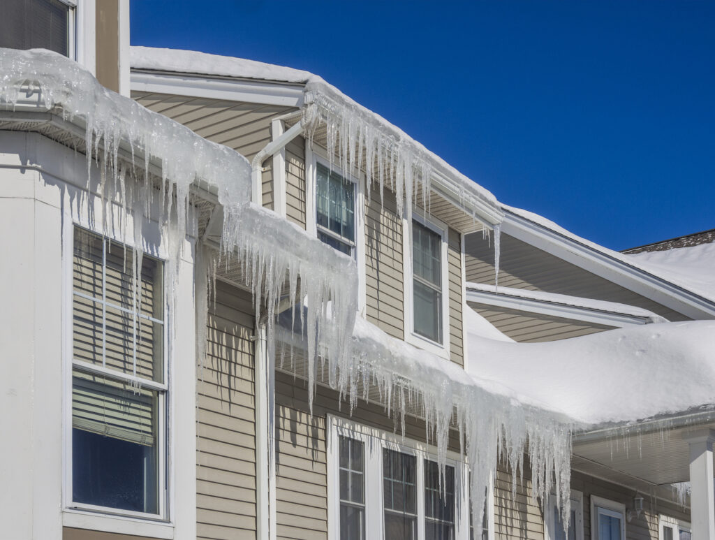 Ice dams and snow on roof and gutters of tan home after bitter cold