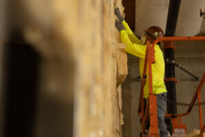 A man in a hard hat installing fiberglass batt insulation.